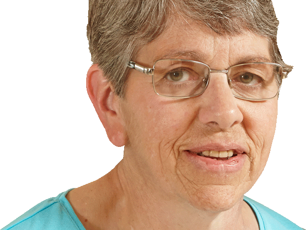 Older woman with short gray hair, glasses, and a blue shirt, looking at the camera and smiling slightly.