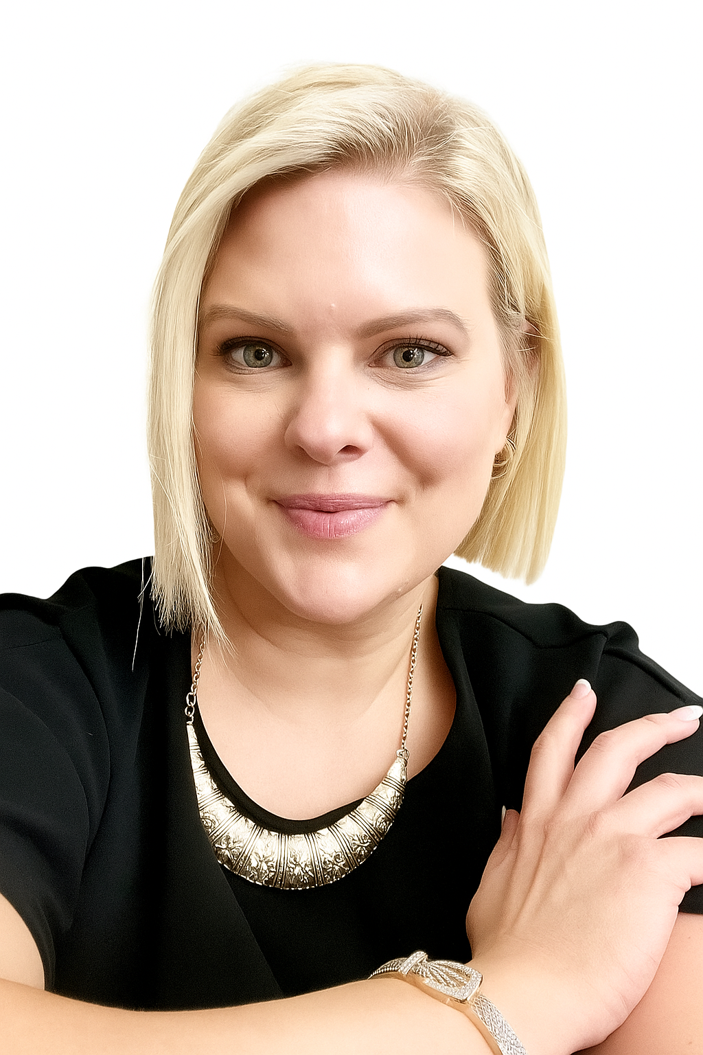 A woman with short blonde hair and light eyes wearing a black top, a large silver necklace, and a watch, smiling with her arms crossed against a white background.