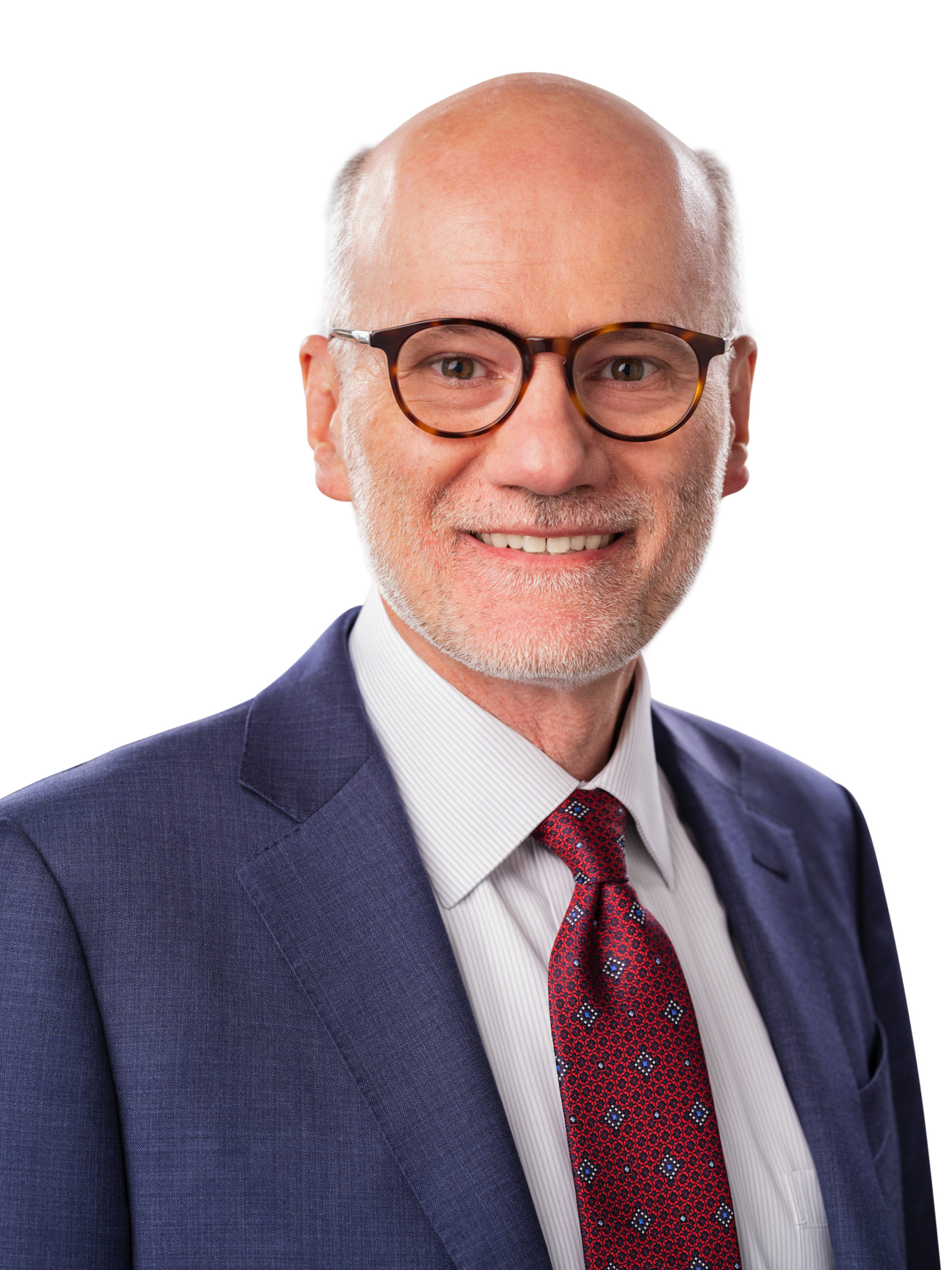 A middle-aged man with glasses, short gray hair, and a beard, wearing a blue suit, white shirt, and red patterned tie, poses against a white background.